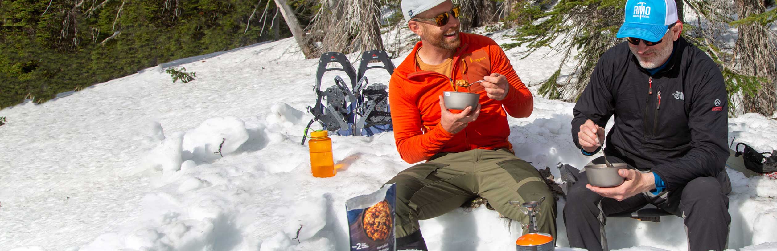 Two people eating freshly cooked RightOnTrek Hearty Beef Bolognese while snowshoeing in the backcountry